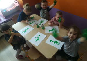 Dzieci odbijają dłoń w farbie na kartce papieru